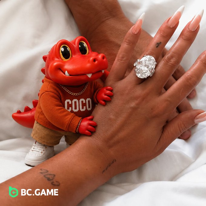 A small red crocodile figurine wearing a 'COCO' sweatshirt and gold chain stands next to a hand displaying a large diamond ring, with the 'BC.GAME' logo in the corner.