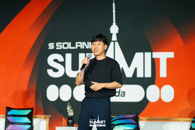 A man in a black t-shirt speaking into a microphone on stage at the Solana Summit in Korea, with the event's branding displayed on a large screen behind him.