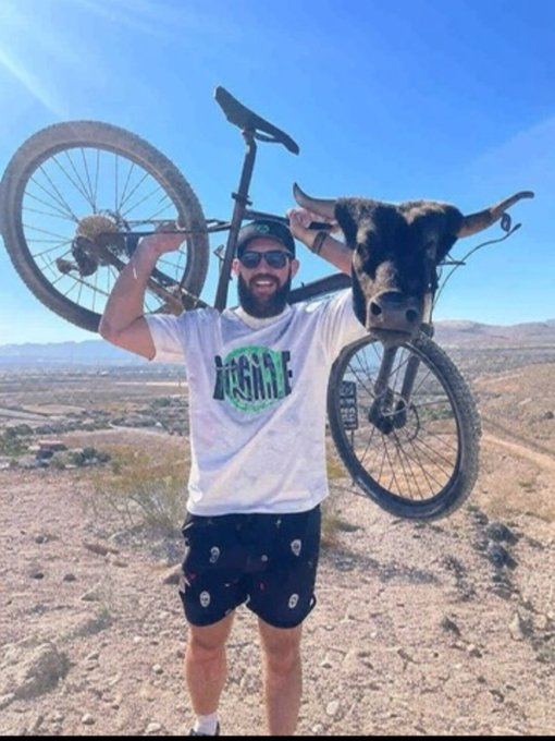 A bearded man in sunglasses lifts a mountain bike overhead with a real bull's head superimposed on the frame, with his shirt reading "BULLISH" — playfully visualizing the "I'm Bullish on $BC" post referencing @bcgame and @BCEngineX.