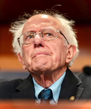 An older man with white hair and glasses, wearing a dark suit and blue striped tie, looks upward with a serious expression.