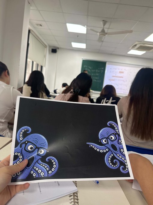 A hand holds up a black card featuring two purple octopus illustrations in a classroom setting.