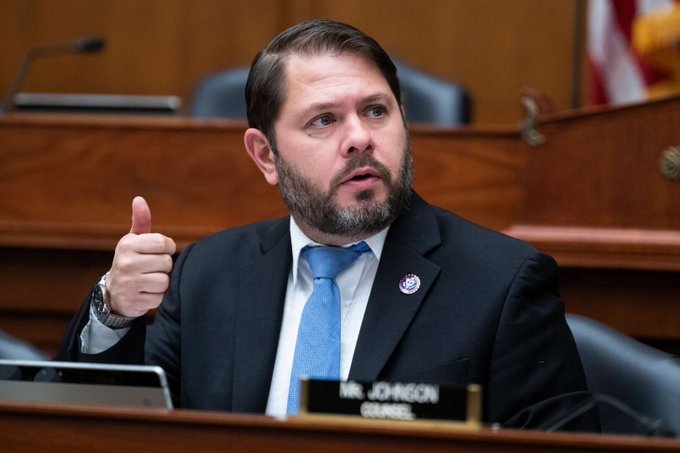 A man in a dark suit and blue tie, identified by the nameplate "MR. JOHNSON COUNCIL," gestures with a thumbs-up while speaking in what appears to be a legislative chamber, visually representing the political figures referenced in the post about the strategic silence surrounding the #ClarityAct.