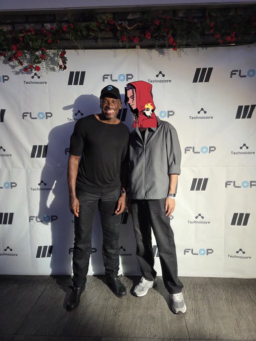 Two people posing in front of a backdrop featuring 'FLOP' and 'Technocore' logos, with one wearing a Spider-Man mask/hood and the other in black casual attire.