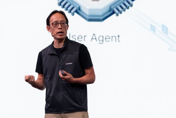 A man wearing glasses and a "mont" branded vest speaks on stage in front of a presentation slide showing the text "User Agent" alongside a microchip graphic. The image appears to capture a tech or crypto industry presentation, aligning with the post's discussion of traditional finance's growing involvement in digital assets.