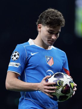 A soccer player in a blue Atlético Madrid jersey holding a Champions League ball during a match.