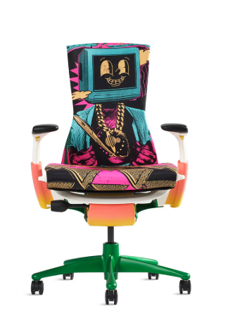 A vibrant, colorful gaming chair features a graffiti-style design with a TV-headed character wearing a gold chain and pink/blue outfit, mounted on a bright green base.