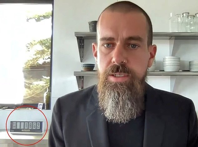 A bearded man in a dark blazer speaking to camera, with a red circle highlighting a digital counter behind him reading '0002'.