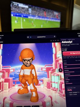 A laptop screen displays an Mii character in a futuristic setting, with a soccer match playing on a TV in the background.