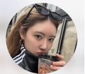 A circular-cropped photo of a young woman with sunglasses on her head drinking from a 'STREET TACO' cup, with a grey sky background.