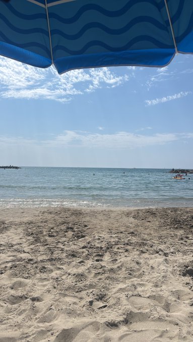 A view of a sandy beach and the ocean from under a blue beach umbrella on a sunny day.