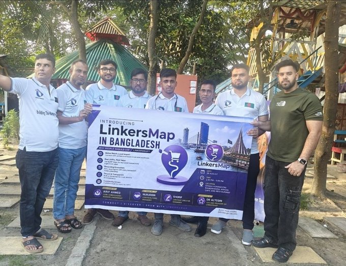 The LinkersMap team, identifiable by their matching branded polo shirts, poses together outdoors while holding a promotional banner that reads "INTRODUCING LinkersMap IN BANGLADESH" alongside contact information for registration. The group stands in front of colorful amusement park structures, visually marking the successful offline launch event in Dhaka mentioned in the post.