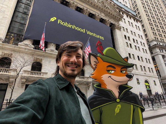A smiling man poses in front of the New York Stock Exchange, where a banner reads "Robinhood Ventures" alongside an American flag, with an animated fox mascot (Robinhood's logo) edited into the frame wearing a green cloak. The image ties to the post's nostalgic reference to the 2020/2021 meme-stock era, when Robinhood became synonymous with retail traders hyping tickers in r/WallStreetBets without needing to drop contract addresses.