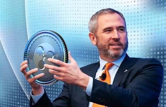 The image features a man wearing a suit, holding up an award or trophy with both hands. He appears to be presenting something to someone else who is also dressed in a suit. The background of the image has a blue and white color scheme, which complements the man's attire. The text on the image reads "@Ripple CEO @bgarlinghouse says the Anti-Crypto Army has officially lost. The courts ruled. And the market is moving forward." This suggests that there might be an event or ceremony related to cryptocurrency or blockchain technology taking place, and the man in the suit could be a representative or participant at this event.