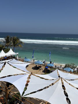 A tropical beach scene with white tent-shaped canopies, palm trees, and the ocean under a clear blue sky.