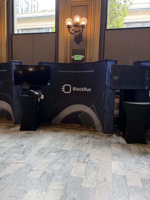 BlockRun's trade show booth display featuring two monitors flanking a banner that reads "Fastest Growing AI Agent Payment Rail" and "BlockRun" at the HF0 Batch S26 residency in San Francisco.