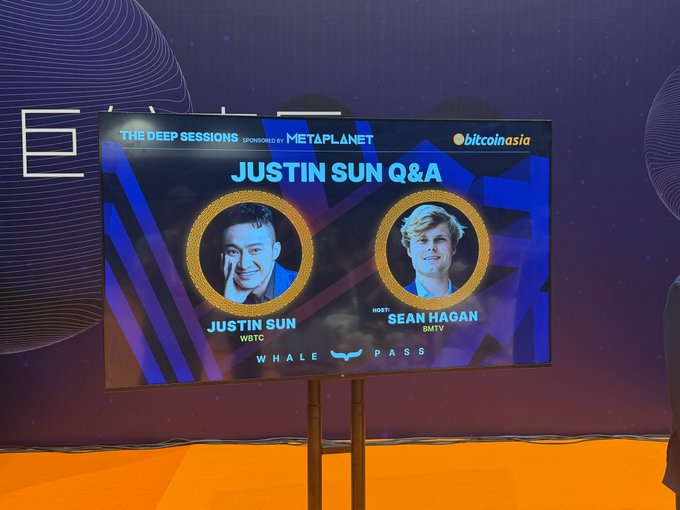 A large screen at the Bitcoin Asia conference displays "JUSTIN SUN Q&A" featuring headshots of Justin Sun (WBTC) and host Sean Hagan (BMTV), sponsored by MetaPlanet, for a fireside chat on the future of digital assets.