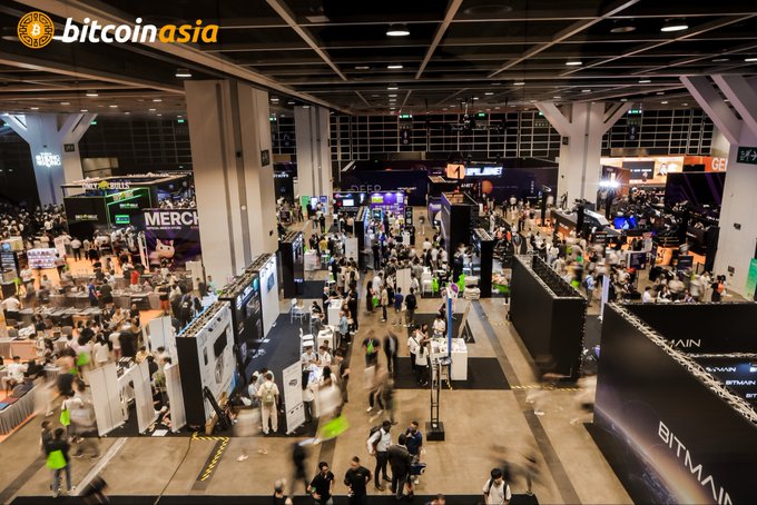 The image shows a packed exhibition hall at Bitcoin Asia in Hong Kong, featuring booths from major crypto mining companies like Bitmain, Merco, and Whatsminer, with crowds of attendees filling the aisles between sponsor displays. The scene perfectly illustrates the post's "PACKED" description, visually confirming the strong turnout at what is billed as Asia's largest Bitcoin conference.