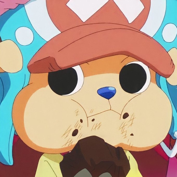 A close-up illustration of a Tony Tony Chopper figurine from the anime One Piece, showing the character's wide-eyed face with a pink X-marked hat and blue antler-like accessories, crumbs on its cheeks as it holds a brown object, fitting the cheerful "Good Morning Everyone" greeting with its cute, awake appearance.