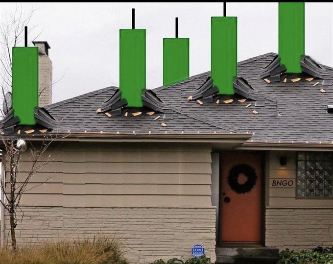 The image shows a row of green candles mounted on top of houses, indicating that Christmas is approaching. There are five house lights and two sets of blue and white wreaths, adding color and festivity to the scene. The overall atmosphere conveys a holiday spirit as houses prepare for the celebration.