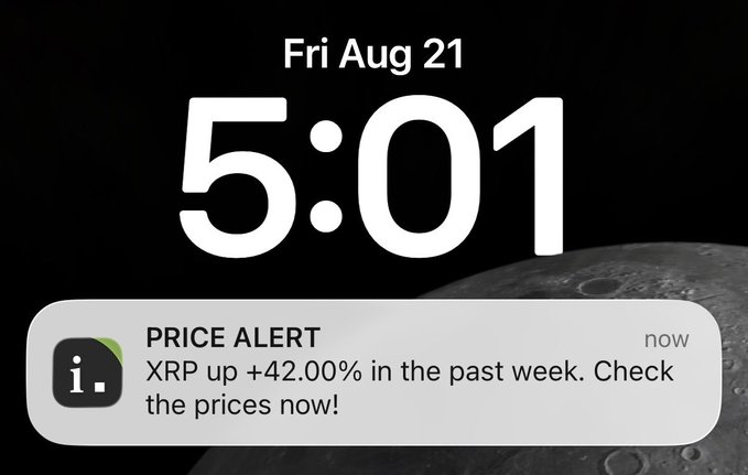 An iPhone lock screen displays "Fri Aug 21, 5:01" with a moon background and a price alert notification reading "PRICE ALERT: XRP up +42.00% in the past week. Check the prices now!"