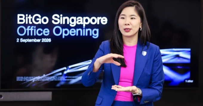 A woman in a blue blazer and pink top gestures while presenting in front of a screen displaying 'BitGo Singapore Office Opening 2 September 2026'.