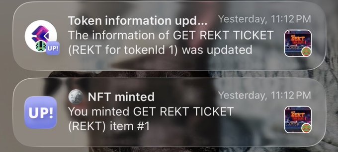 A smartphone notification screen displaying two alerts from UP! at 11:12 PM: 'Token information upd...' stating 'The information of GET REKT TICKET (REKT for tokenId 1) was updated', and 'NFT minted' confirming 'You minted GET REKT TICKET (REKT) item #1'.