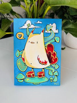 A small canvas painting featuring a cute white creature with red horns against a blue sky with clouds and green plant-like elements, sitting on a windowsill.