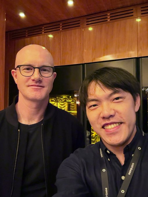 The image features two men posing together, both wearing glasses and smiling at the camera. They are standing close to each other, with one man slightly behind the other. The background of the photo shows a wooden wall, which adds an interesting visual element to the scene. The caption accompanying the image reads "Great lunch with Brian Armstrong in New York. Finally got to meet the team @ coinbase in person. Back to building. Can't wait to share what's next." This suggests that they are at a restaurant or another location where they have recently had a meal, and they are now back to their daily activities.