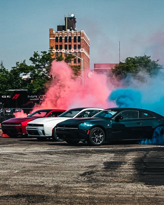 The image features a row of cars parked next to each other with smoke coming from their tires, creating an interesting visual effect. The cars are positioned at various angles, showcasing different perspectives of the scene. In the background, there's a building that adds depth to the image and provides context for the parking lot setting. The caption provided in the image seems unrelated to the actual photo but is meant to be informative or entertaining.