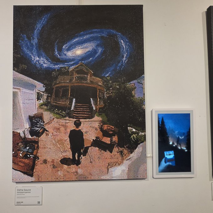 An art gallery display featuring a large painting titled '#thephysicalexperience' by Delta Sauce, depicting a figure standing before a house with a swirling cosmic galaxy overhead, alongside a smaller framed digital piece.