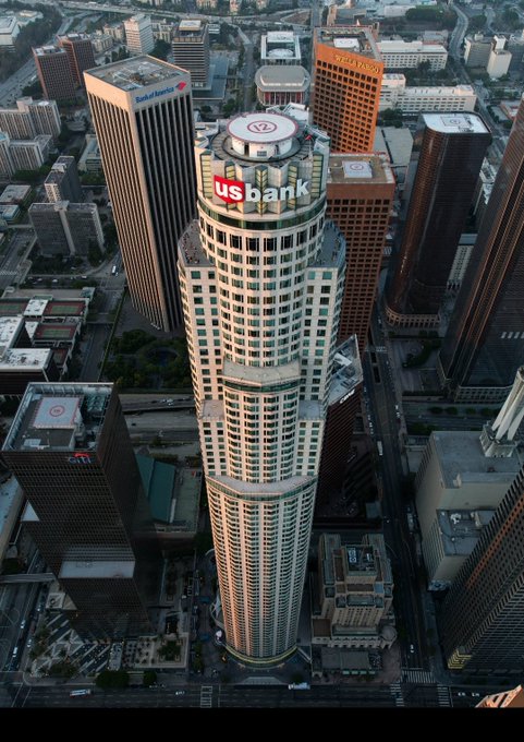 Aerial view of downtown Los Angeles featuring the cylindrical U.S. Bank Tower with its prominent 'usbank' sign, surrounded by other skyscrapers including the Bank of America building.