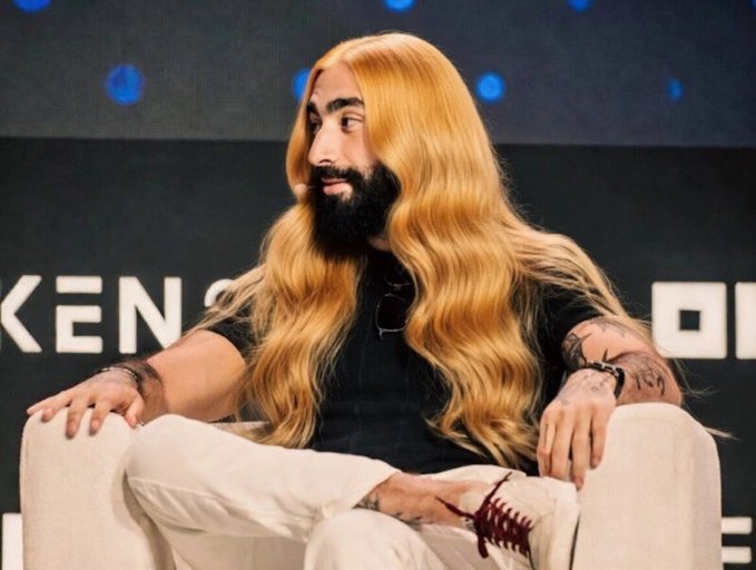 The image features a man with long blonde hair sitting in a chair, wearing a black shirt and white pants. The caption of the photo reads "Someone check on this #ZEC guy He has been tweeting every minute." This suggests that the man is actively engaging with his followers by sharing updates or thoughts about something he's interested in.

The image also contains text that reads "Kenzen" and "Owen", which could be related to a brand, product, or event. The presence of these texts indicates that there might be some connection between the man and the content being shared on social media platforms.