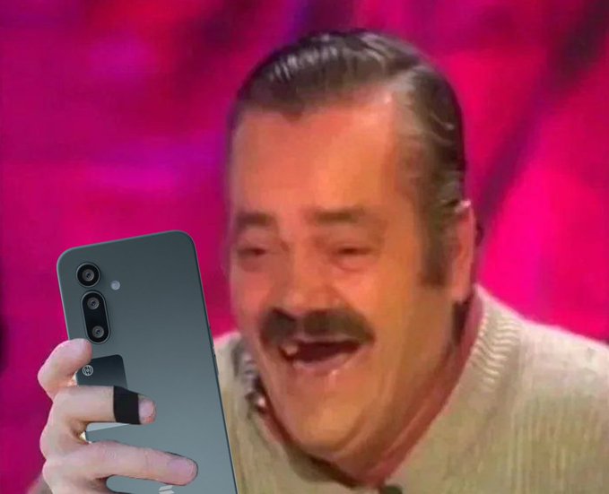 A man with a mustache laughs heartily while holding up a gray smartphone, set against a bright pink background.