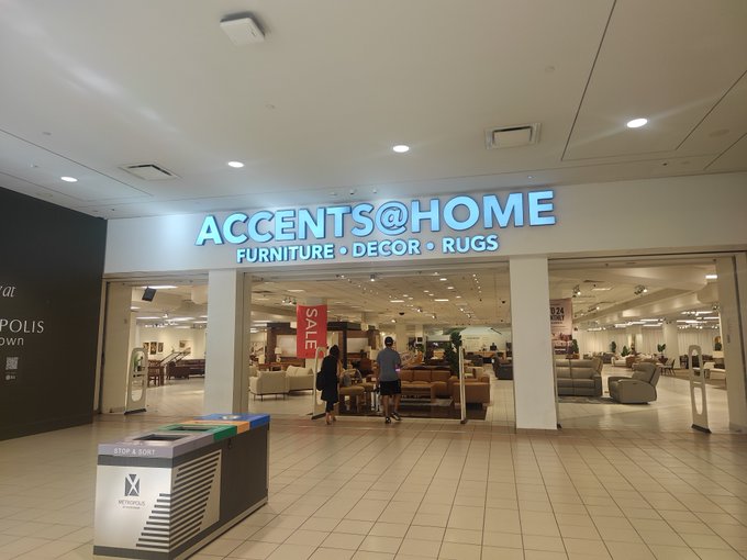 The storefront of 'ACCENTS@HOME' specializing in 'FURNITURE • DECOR • RUGS' is shown inside a mall, with a red 'SALE' sign visible in the entrance and customers browsing inside.