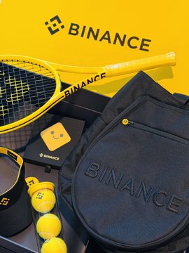The image features various tennis-related items, including a yellow tennis racket, a black tennis bag, and several tennis balls. The main focus of the image is a tennis ball holder that contains multiple tennis balls. The Binance Dragon Boat Festival gift box has been opened, revealing its contents.