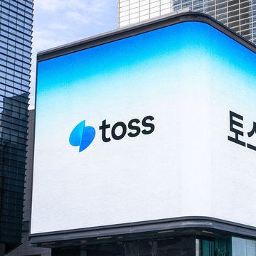 The image shows a large white building with a blue logo that reads "TOSS" on top of it, along with some text below it. The building appears to be located near a tall skyscraper or office building. In the background, there is another building visible in the distance. The post includes information about a new cross-border stablecoin called TORS (Test) and mentions that South Korea's Toss Bank has been collaborating with Solana to test this stablecoin for its 15M customers.