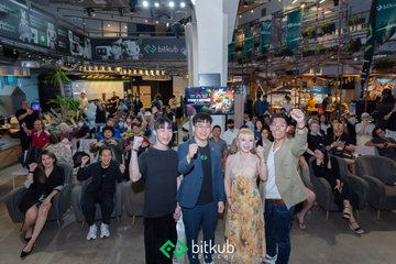 The image shows a group of people standing next to each other with their arms raised in celebration or victory. They are posing for a photo, likely at an event like Bitkub x Abstract: Meetup. The atmosphere appears to be joyful and positive as they gather together after the conclusion of the event.