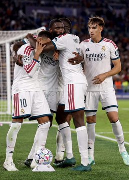 Real Madrid players wearing white jerseys featuring the "Emirates FLY BETTER" sponsor and the number 10 celebrate on the pitch following a dramatic late comeback. The image visually captures the team's triumph referenced in the post, where Madrid overcame a 3-1 deficit with three goals in the final 10 minutes to win their UCL match.