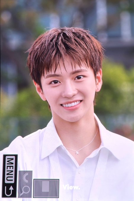 A portrait-style image of a smiling young man with short brown hair wearing a white collared shirt and a star necklace. The image has UI overlays including 'MENU', 'View.', and a magnifying glass icon, indicating it's a digital photo viewer interface.