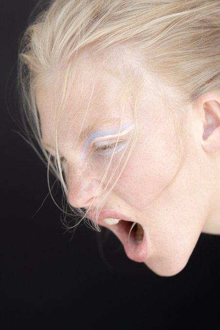 A pale-skinned person with wet blonde hair, blue eyeshadow, and an open mouth tilts their head down against a black background. The raw, avant-garde portrait mirrors the post's commentary on digital art value, embodying the unfiltered, provocative aesthetic associated with "ATH (All-Time High)" NFT collections.