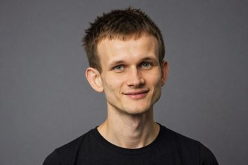 A young man with short, light brown hair and blue eyes smiles slightly while wearing a black t-shirt against a plain gray background. The image appears to be a portrait of Vitalik Buterin, the Ethereum co-founder referenced in the post about his recent $1.6 million wallet transfer.
