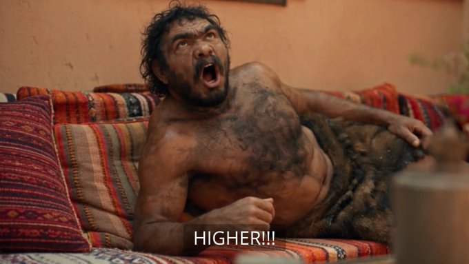 A still from The Greasy Strangler showing a hairy, shirtless man screaming on a couch with the subtitle "HIGHER!!!".
