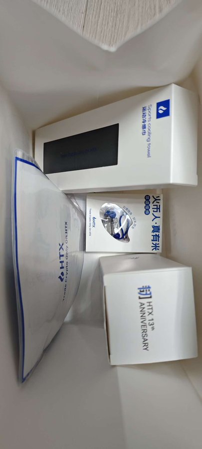 Several boxes and packages from the brand 'HTX' are stacked on a shelf, including ones labeled 'Sports Cooling Towel' and 'HTX 13th ANNIVERSARY' with Chinese text.