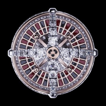 A close-up image of a circular piece of jewelry, possibly a ring or pendant, featuring a geometric design with diamonds and red gemstones set in a metallic band.