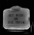 A letterboard sign on a dark background reads 'GET RICH OR DIE TRYIN'.