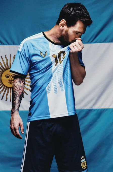 An emotional soccer player in an Argentina jersey pulling it over his face, standing in front of the Argentine flag.