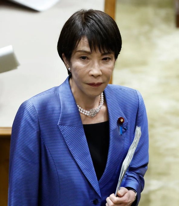 A portrait of a Japanese woman with short black hair, wearing a blue striped blazer and a pearl necklace, holding a folded fan.