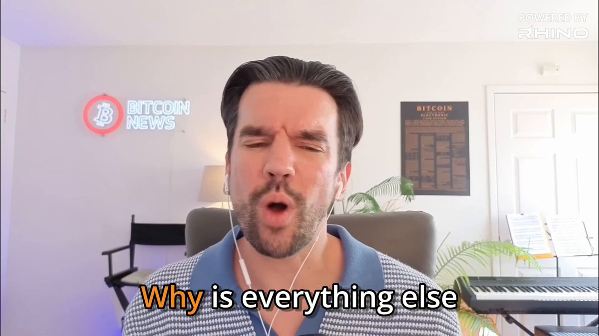 The image shows a man wearing headphones with his eyes closed while sitting at a piano keyboard. The background features a poster of Bitcoin News logo, which is located above the man's head. Below this, there are two lines of text that read "Why is everything up while Bitcoin is languishing? @Excellion thinks people are rebalancing into AI IPOs like SpaceX and Anthropic, chasing the trendy thing." The man appears to be in a room with a piano keyboard nearby, suggesting he might be playing music or taking a break from work.