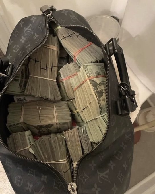 A Louis Vuitton duffel bag is filled with stacks of US dollar bills banded together with rubber bands.