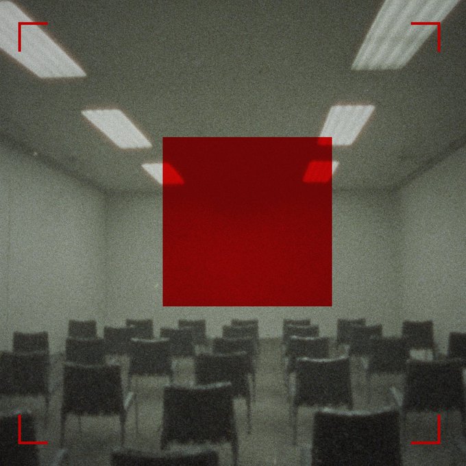 A dimly lit room with rows of chairs and ceiling lights, featuring a large red square obscuring the center of the image, with red corner brackets framing the scene like a camera viewfinder.
